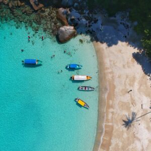 Nos packs de voyage sur mesure. Vue aérienne d'une plage paradisiaque avec des petits bateaux, offrant un cadre idyllique pour des vacances de rêve.